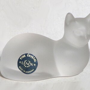 Puede incluir: Una figura de gato de cristal esmerilado. El gato está en posición de descanso con las orejas levantadas. Una pegatina azul y blanca en el lateral dice "FINE CRYSTAL LENOX MADE IN GERMANY".
