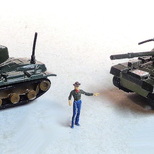 Puede incluir: Dos tanques militares de juguete, uno verde y otro verde oscuro, con detalles y orugas. El tanque más grande tiene el texto "8129 CHIEFTAIN" impreso en el lateral.