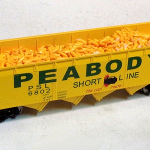 May include: Yellow model train car with the words "PEABODY SHORT LINE" and "The coal route" printed on the side. The car is filled with yellow plastic pellets.