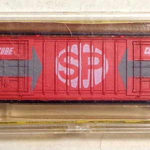 May include: A red boxcar model train with the words "Southern Pacific" and "Boxcar" printed on the side. The car has a white "SP" logo with a dollar sign in the middle.