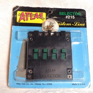 May include: A black Atlas Selector #215 in a blue and black package. The selector has four green switches labeled A, B, C, and D. The package includes a clear plastic dome with small metal components. The text "ATLAS SELECTOR" is visible.