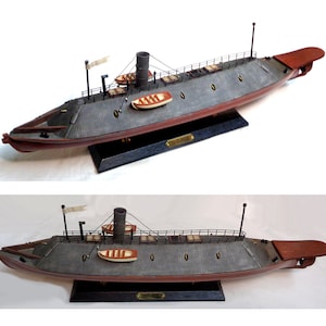 May include: A detailed model of a Civil War-era ironclad warship. The model features a gray hull with red trim, a central smokestack, and small lifeboats. The model is mounted on a black base with a nameplate.