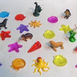 以下が含まれることがあります： ヒトデ、タコ、ウミガメ、セイウチなど、カラフルなプラスチック製の海の生き物の玩具のコレクション。貝殻とペンギンもいくつかあります。