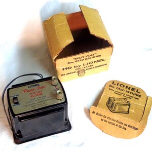 May include: A black Lionel "Recti-Volt" Type 0150 Rectifier in its original box. The box is brown with white text and a picture of a train engineer. The rectifier has a forward and reverse switch, a track switch, and a label that reads "Output 6-12 VDC 1.5 A".