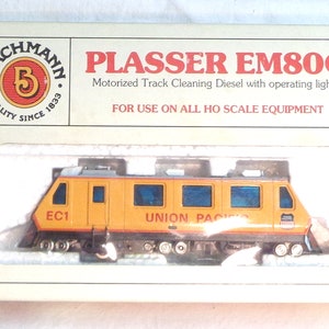 May include: A yellow and black Bachmann Plasser EM80C motorized track cleaning diesel model train with operating lights. The train is labeled "EC1" and "UNION PACIFIC".