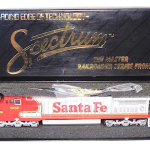 May include: A model train locomotive in a box. The red and silver train car has the words "Santa Fe" printed on the side. The box is black with gold lettering that reads "Spectrum" and "The Master Railroader Series from Bachmann."