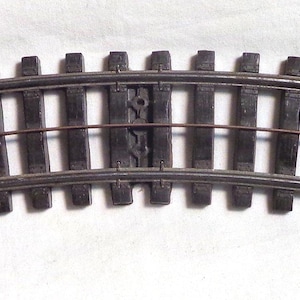 May include: A curved piece of model train track made of brown plastic. The track has metal rails and is designed for use with HO scale model trains.