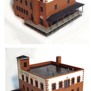May include: A model of a brick building with a black roof and a sign that reads "Lion-Milk Milk Products". The building has a porch with a black railing and a white roof.