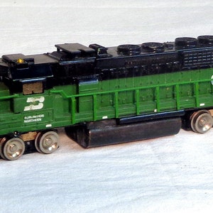 May include: Green and black model train locomotive with the number 8336 printed on the side. The locomotive has a black cab and a green body with a number 3 printed on the side.