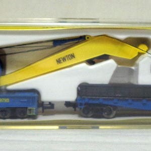 May include: A blue and yellow Santa Fe crane train set in a clear plastic case. The crane arm is yellow with the name "NEWTON" printed on it. The train car is blue with the words "Santa Fe" printed on the side.