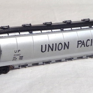 Puede incluir: Un vagón de tren modelo plateado con las palabras "UNION PACIFIC" impresas en el lateral. El modelo tiene ruedas negras y un techo negro. El modelo también tiene las letras "UP" y el número "21382" impresos en el lateral.