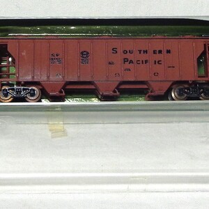 May include: A model train car in a clear plastic case. The car is a reddish-brown color and has the words "SOUTHERN PACIFIC" printed on the side. The case is open, revealing a green interior.