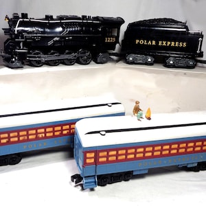 May include: A black Polar Express steam locomotive with the number 1225, a coal tender, and two blue passenger cars with white roofs and yellow windows. A small figurine sits on the roof of one passenger car near a tiny orange campfire accessory.