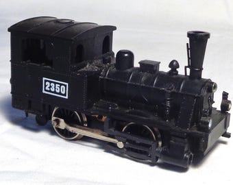 Op de afbeelding: Een zwart modeltrein met het nummer 2350 in een wit kader. De trein heeft een schoorsteen, een cabine en meerdere wielen. Dit vintage speelgoed is een klassiek model.