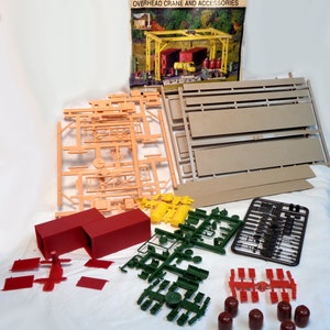 May include: A model kit for an overhead crane and accessories. The kit includes plastic parts in various colours, including orange, red, green, and black. The box art features the text "North Star Glass Company Overhead Crane and Accessories".