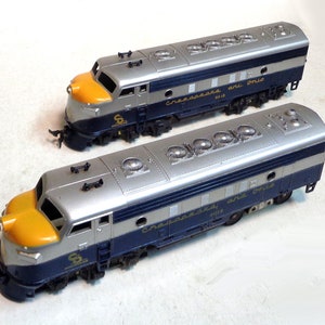 May include: Two silver and blue model train engines with yellow noses. The engines are labelled "Chesapeake and Ohio" and have a number "8018" on the side.