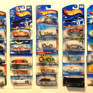 Könnte beinhalten: Eine Sammlung von 10 Hot Wheels Spielzeugautos in ihrer Originalverpackung. Die Autos sind alle in verschiedenen Farben und Stilen, darunter ein weißer Hot Rod, ein roter Pickup, ein grüner Traktor und ein blaues Rennwagen. Die Verpackung ist blau und trägt das Hot Wheels Logo.