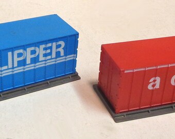 Op de afbeelding: Twee speelgoed-containers, een blauwe met de tekst "CLIPPER CCL 4'43'" en de andere rood met de tekst "a c L".