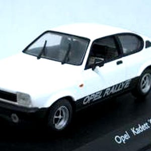 May include: A white Opel Kadett C GTE model car with black accents and the text "Opel Rallye" on the side. The miniature car sits on a black base. The model has a detailed interior and windshield wipers.