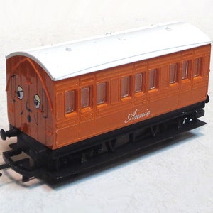 May include: An orange and white toy train car with a face and the name "Annie" printed on the side.