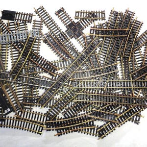 Può includere: Un insieme di binari di treni modello, tra cui pezzi dritti, curvi e di incrocio. I binari sono neri con rotaie color ottone, disposti su una superficie bianca. Per gli appassionati di modellismo ferroviario.