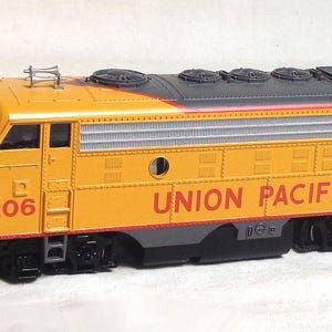 May include: A yellow and gray model train with the text "UNION PACIFIC" in red. The model train has the number "1206" on the side. The train has black wheels and a detailed design.