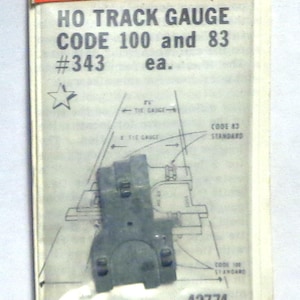 May include: Package for HO track gauge code 100 and 83, with the text "#343 ea." and a diagram. The package is orange and white with the brand name "Kadee". The product is a model train accessory.