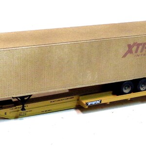 Op de afbeelding: Een gele modeltreinwagen met een bruine vrachtcontainer erop. De container heeft de tekst "XTRA INTERMODAL" op de zijkant.