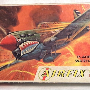 May include: A vintage model airplane kit box featuring a colorful illustration of a P-40E-1A Warhawk fighter plane in flight. The box is labeled "Airfix 1/72 Constant Scale Kit by Craft Master".
