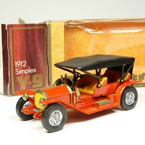 May include: A red 1912 Simplex toy car model with a black canvas top, yellow seats, and black wheels. The car is in its original box, which is labeled "1912 Simplex Y-9".