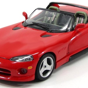 Puede incluir: Un modelo de coche deportivo Dodge Viper rojo convertible con detalles negros y un interior negro. El coche tiene un parabrisas negro y ruedas negras con radios plateados.