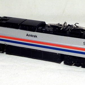 May include: A silver and black Amtrak model train with red and blue stripes. The number 951 is visible on the side. The word "Amtrak" is printed on the side of the train.