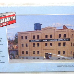 Puede incluir: Un kit de maqueta de un almacén de ladrillo con una torre de agua en el techo. La imagen de la caja muestra el edificio con el texto "Reliable Warehouse & Storage" en la parte delantera. El kit forma parte de la serie Cornerstone de Walthers.