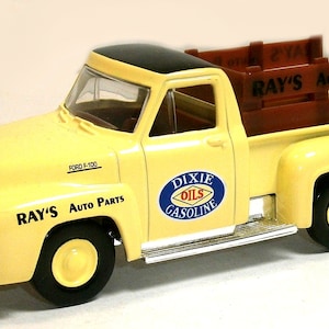 Könnte beinhalten: Ein gelber Ford F-100 Pickup mit einer Holzpritsche und einem schwarzen Dach. Der LKW hat ein "Dixie Oils Gasoline" Logo an der Seite und "Ray's Auto Parts" auf der Ladefläche und der Seite.