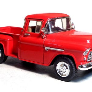 Puede incluir: Modelo de camioneta vintage rojo brillante con detalles cromados. El camión clásico presenta una parrilla delantera detallada, faros y espejos laterales. El camión tiene neumáticos negros y una caja de carga roja.