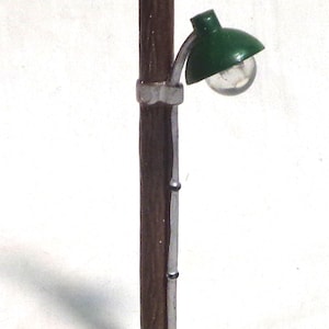 May include: A miniature wooden lamp post with a green lampshade and a clear glass bulb. The post is on a white base.