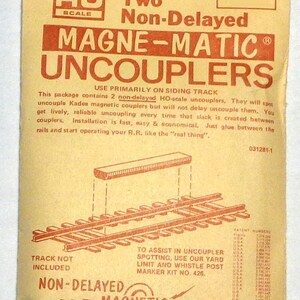May include: A vintage package for Kadee HO scale 312 Magne-Matic Non-Delayed Uncouplers. The package is tan with red text and illustrations, including a diagram of train tracks and the words "Non-Delayed Magnetic Uncoupling."