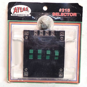 May include: A black plastic Atlas Model Railroad Co. #215 Selector switch with green switches. The packaging is black with white text and a red, white, and blue logo.
