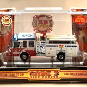 May include: A die-cast Code 3 Fire Engine model in a clear plastic display case. The fire engine is red, white, and blue with the text "KB toys" and "Code 3 Fire Engine". The packaging includes a "Limited Edition" label and a serial numbered certificate.