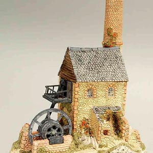 Puede incluir: Una maqueta en miniatura de un molino de piedra con una rueda hidráulica, chimenea y balcón. El edificio tiene un tejado de tejas grises, paredes de piedra amarilla y una chimenea de ladrillo. Flores rojas y follaje verde.