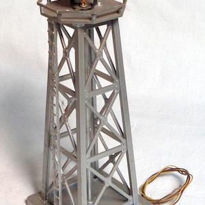 May include: A silver model radio tower with a spotlight. The tower has a lattice structure and a small ladder. A wire extends from the base. The tower is approximately 25 cm tall.