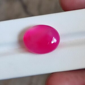 Puede incluir: Una gema redonda y vibrante de color rosa intenso, con una superficie pulida y brillante. La gema se muestra sobre un fondo blanco, resaltando su color y forma. Adecuada para la creación de joyas.