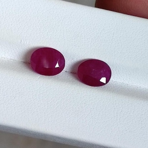 Peut inclure: Deux pierres précieuses rubis ovales et facettées. Les rubis sont d'un rouge profond et riche, avec une légère variation de ton. Elles sont présentées sur une surface blanche, mettant en valeur leur brillance et leur clarté. Idéal pour la joaillerie.