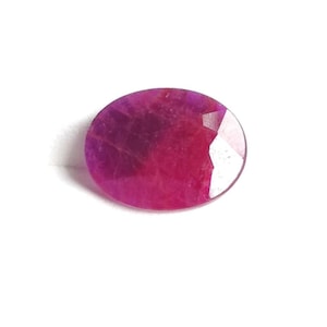 May include: An oval-shaped, faceted ruby gemstone. The gem has a deep red-pink colour with a polished, reflective surface. The gemstone is set against a white background, highlighting its colour and clarity.