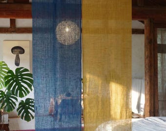 Puede incluir: Dos cortinas largas y rectangulares de lino, una azul oscuro y otra amarillo dorado, cuelgan de una barra en una habitación rústica. Las cortinas tienen un aspecto texturizado y la luz natural las atraviesa. Se ve una impresión artística de setas.