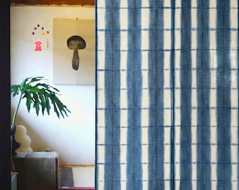 Puede incluir: Cortina de tela a rayas azules y blancas colgada en una puerta. La cortina tiene un aspecto texturizado con rayas verticales. El fondo muestra una habitación con techo de madera, obras de arte y alfombras coloridas.