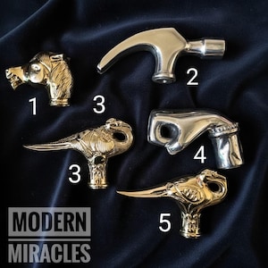 May include: Five metal cane handles labeled with numbers. Item 1 is a gold-colored horse head. Item 2 is a silver-colored hammer head. Item 3 and 5 are gold-colored birds. Item 4 is a silver-colored hand gesture. Text reads MODERN MIRACLES.