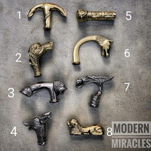 May include: Collection of eight decorative cane handles in various designs. Includes handles shaped like an anchor, dog head, lion, wolf, and a reclining lion. The handles are made of gold and silver-colored metal.