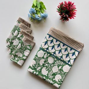Puede incluir: Un mantel con estampado floral verde y blanco y servilletas a juego. El mantel tiene un borde a rayas marrón y blanco y un diseño festoneado azul y blanco. Las servilletas tienen un borde a rayas marrón y blanco.