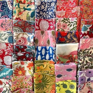 Può includere: Una collezione di quadrati di tessuto piegati con vari motivi floreali e geometrici. I tessuti presentano una gamma di colori, tra cui rosso, blu, rosa e giallo. Alcuni disegni includono fiori, foglie e motivi di pesci.